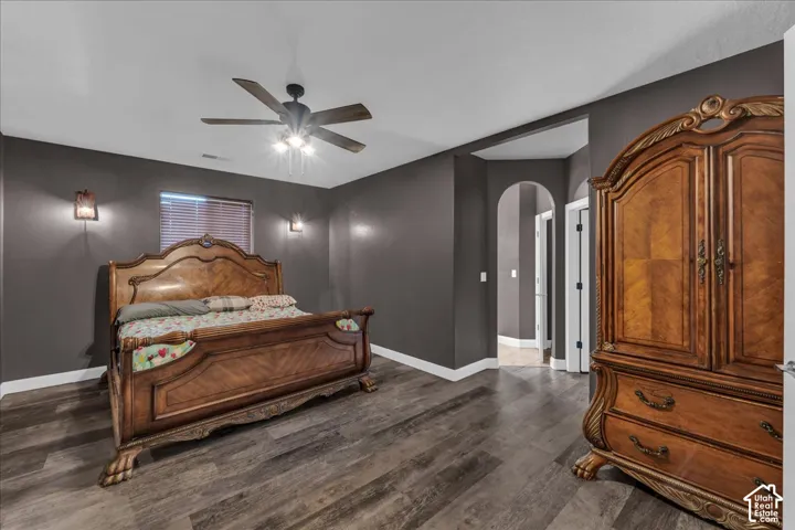 Wood-finish flooring, ceiling fan with integrated lighting, wall-mounted sconces, and an arched doorway