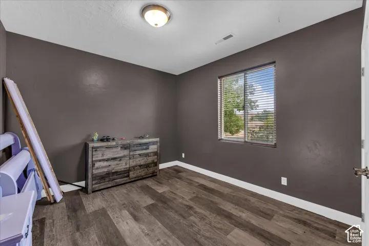 Wood-finish flooring with a neutral wall color, featuring a window with blinds, and an overhead flush-mount light fixture