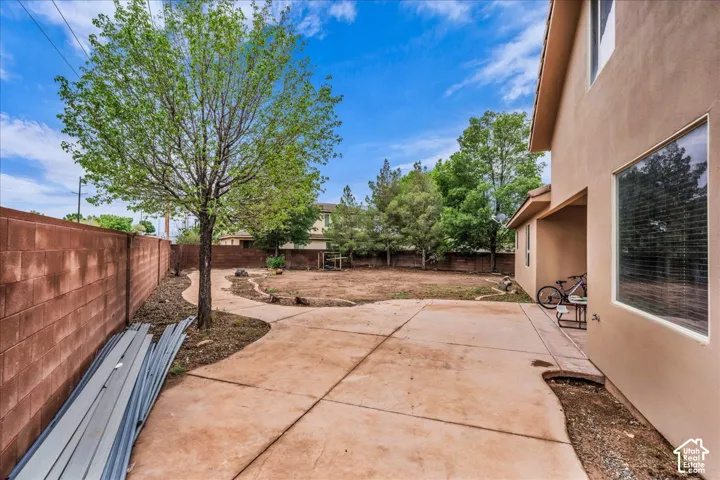 Expansive backyard featuring a concrete patio, mature tree, and block wall fencing