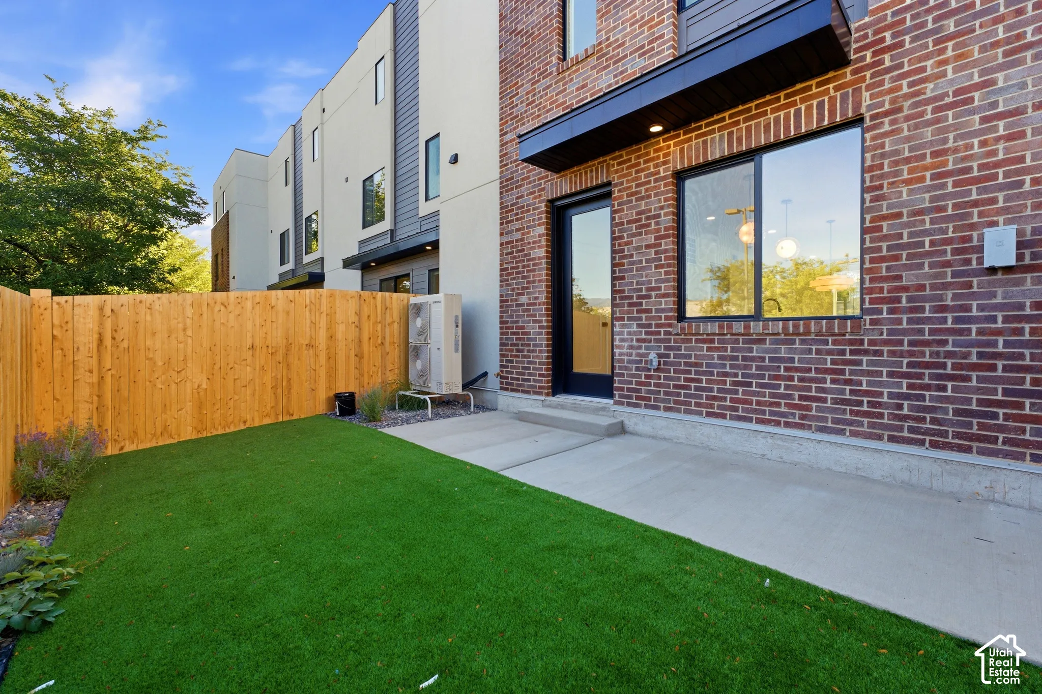 Enclosed patio featuring artificial turf, a concrete pad, and a wood privacy fence