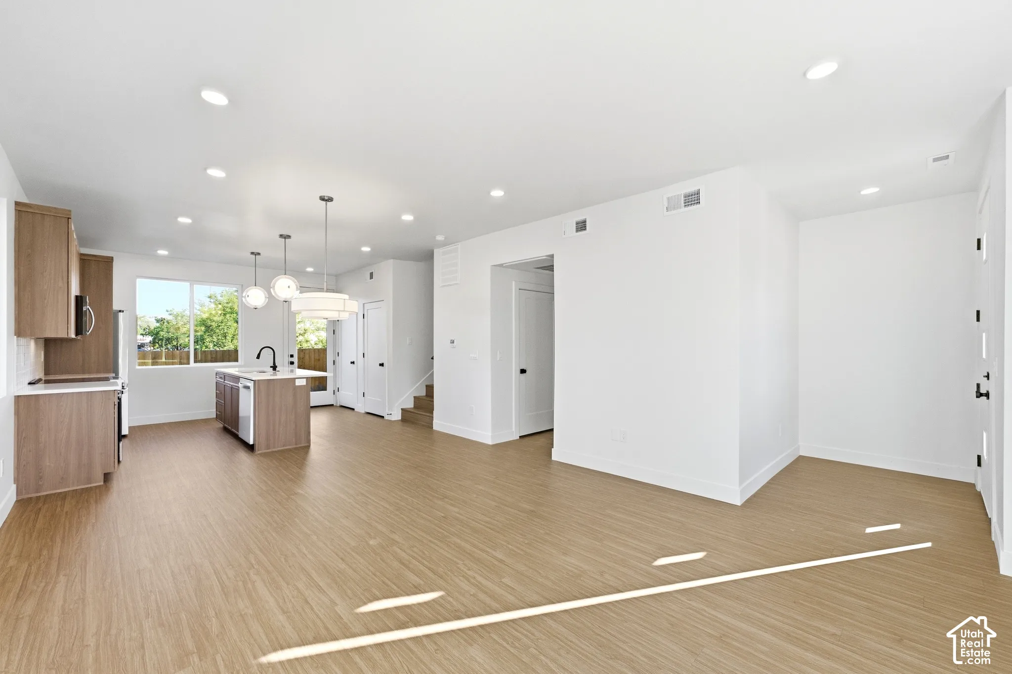 Open-concept living space featuring LVP flooring, recessed lighting, a modern kitchen island with pendant lighting, and light wood-tone cabinetry