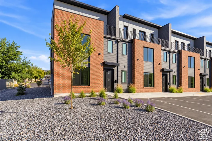 Modern exterior featuring brick and panel siding, large windows, an attached balcony, and a gravel landscape
