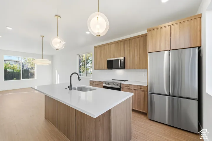 Modern kitchen featuring a large central island with a sink, stainless steel appliances, wood-finish cabinetry, white tile backsplash, and recessed lighting