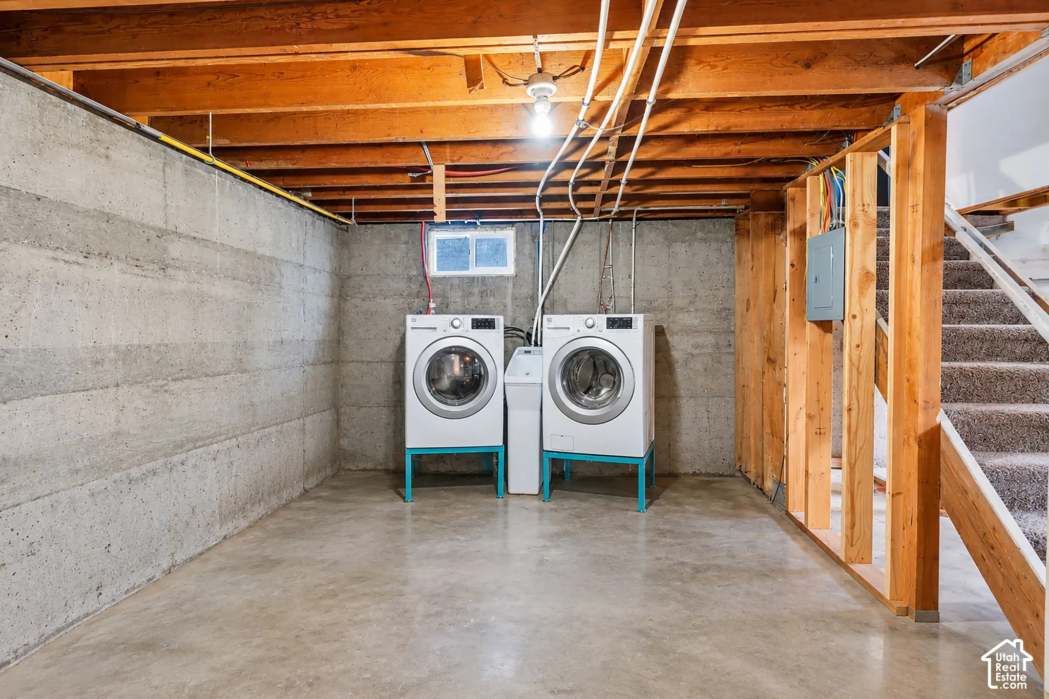 Unfinished basement with concrete flooring and exposed ceiling joists, featuring a utility sink and a small window