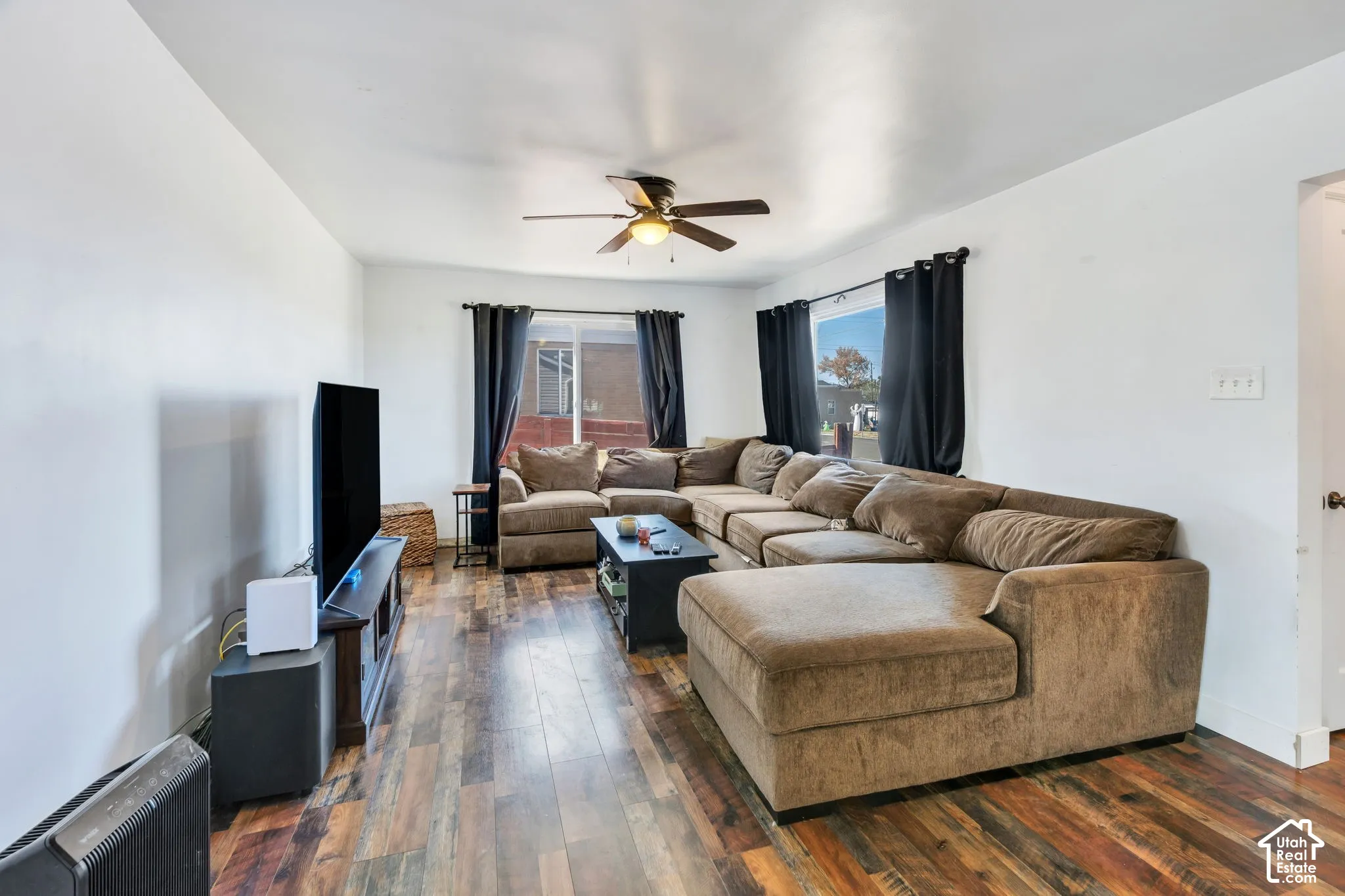 Expansive living area featuring wood-finish flooring, white walls, and a ceiling fan with integrated lighting