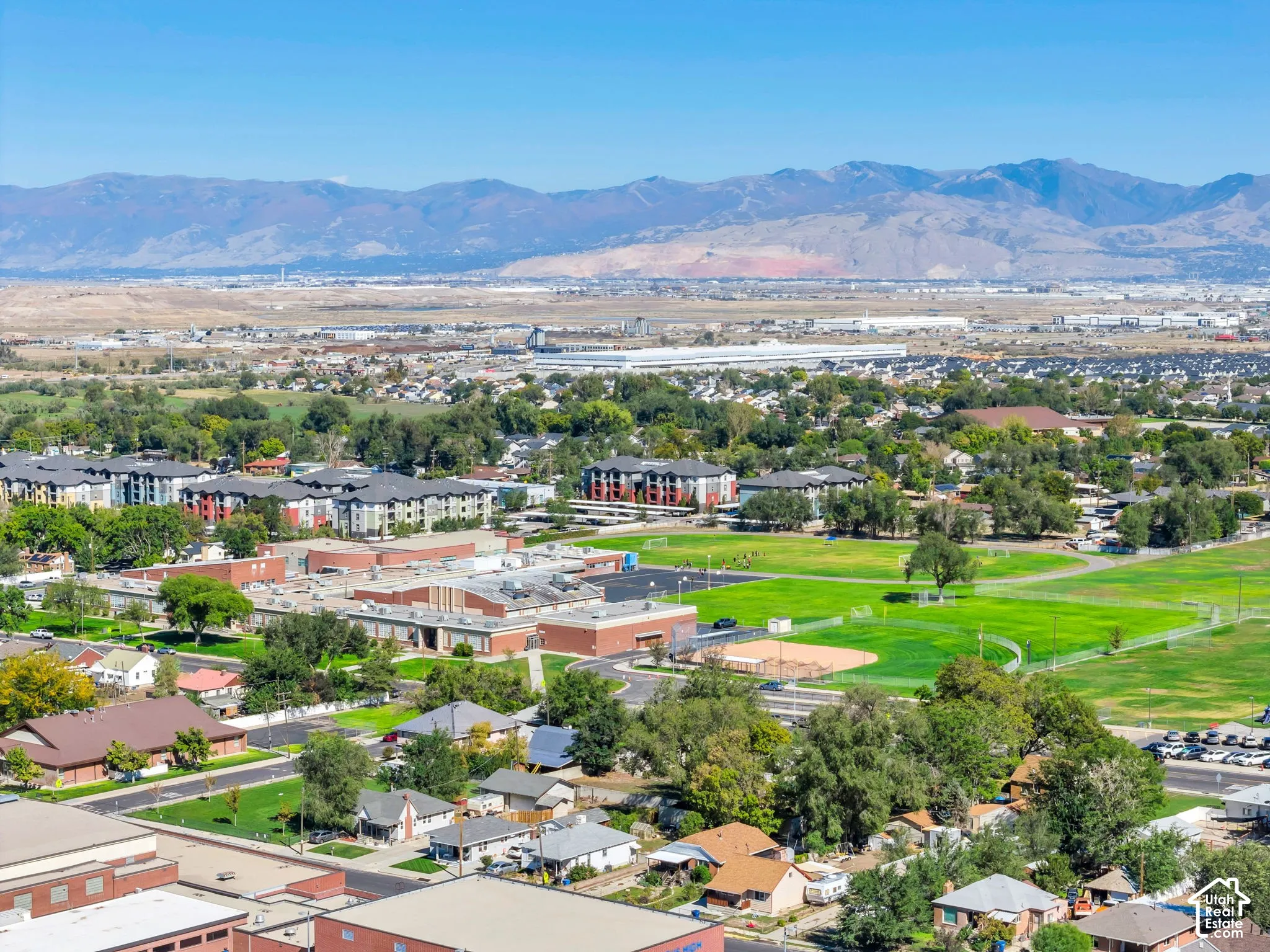 Expansive urban landscape with distant mountains, featuring residential buildings, green spaces, and a sports field
