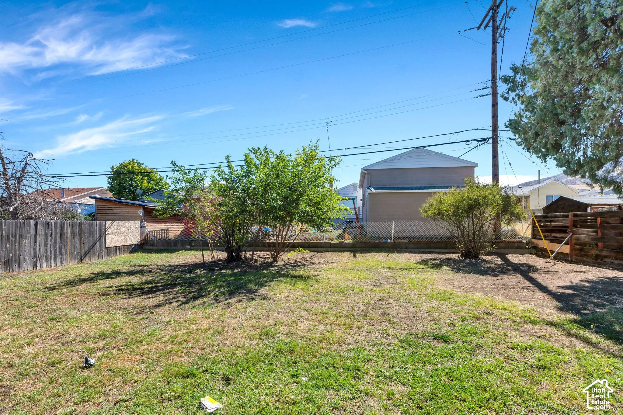 Expansive outdoor space featuring a large lawn area, established shrubbery, and wood fencing