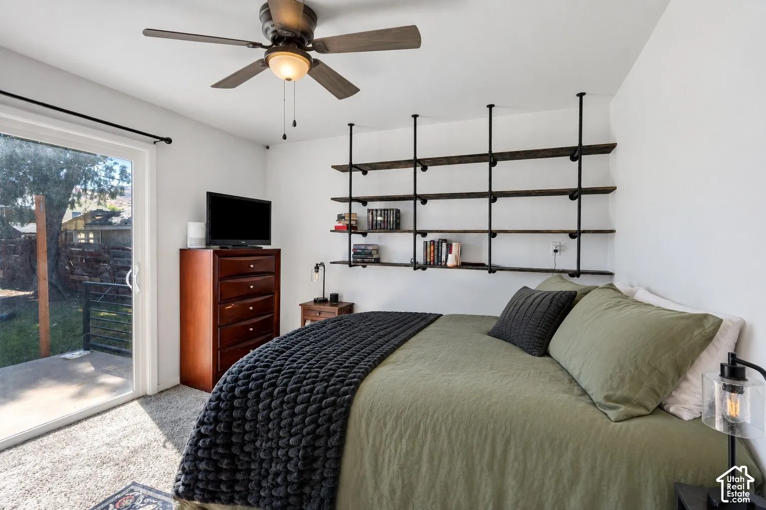 Sliding glass door, ceiling fan with integrated lighting, wall-mounted shelving unit, and textile flooring