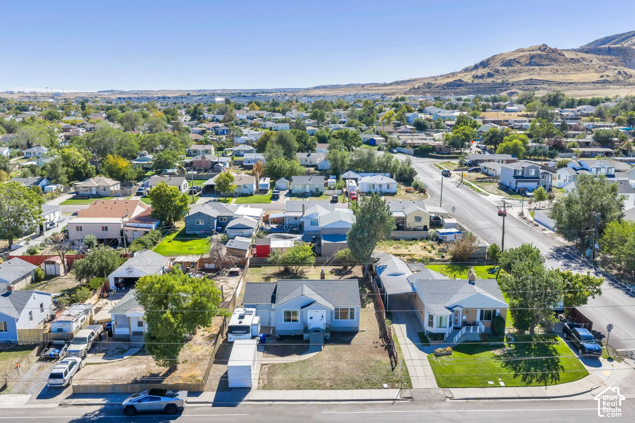 Aerial perspective of a neighborhood with diverse housing styles, mature trees, and a distant mountain backdrop