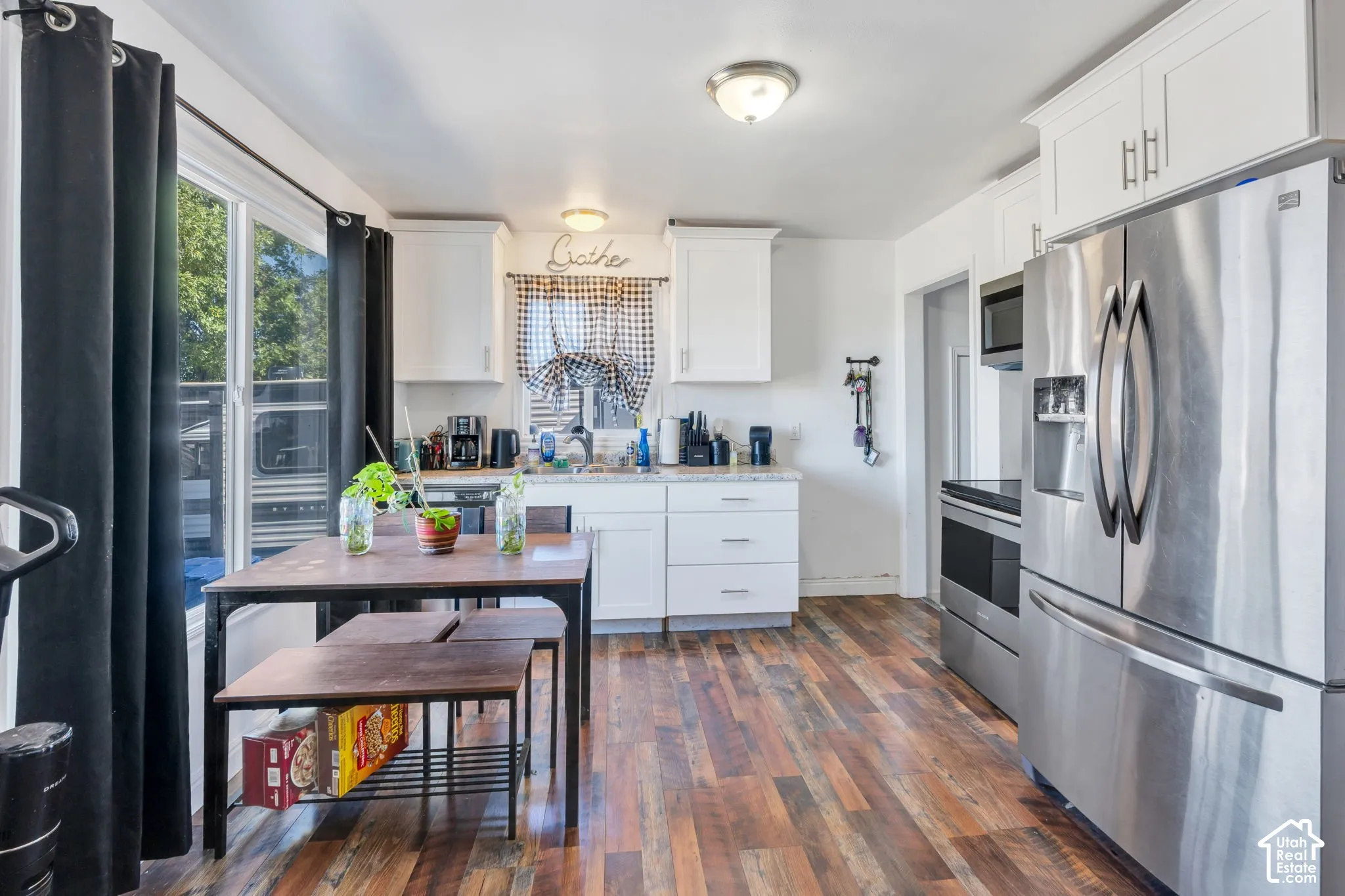 White cabinetry with modern hardware, stainless steel appliances, wood-finish flooring, and a bright window