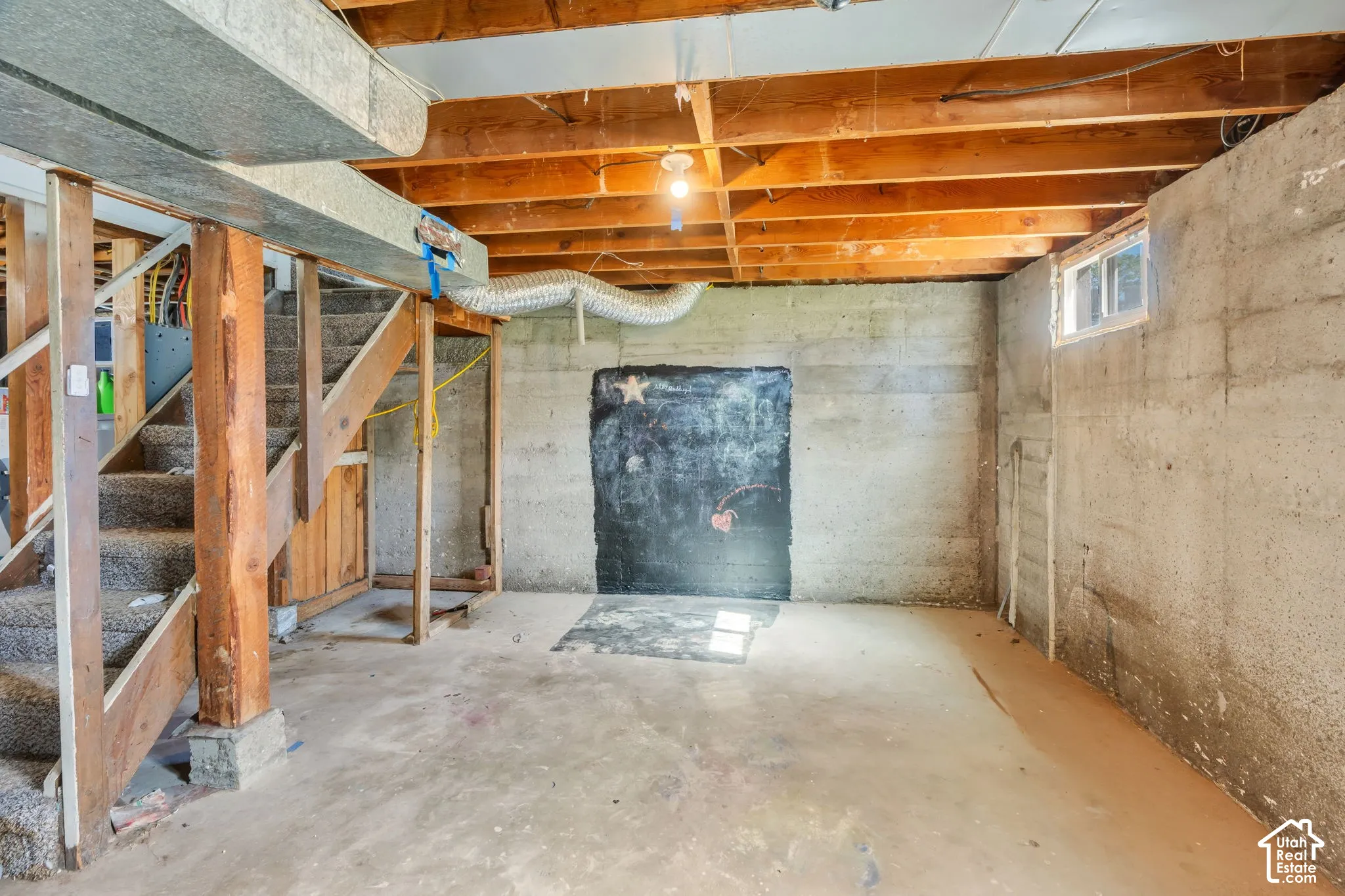 Concrete flooring, exposed wooden ceiling joists, concrete wall construction, and a window providing natural illumination