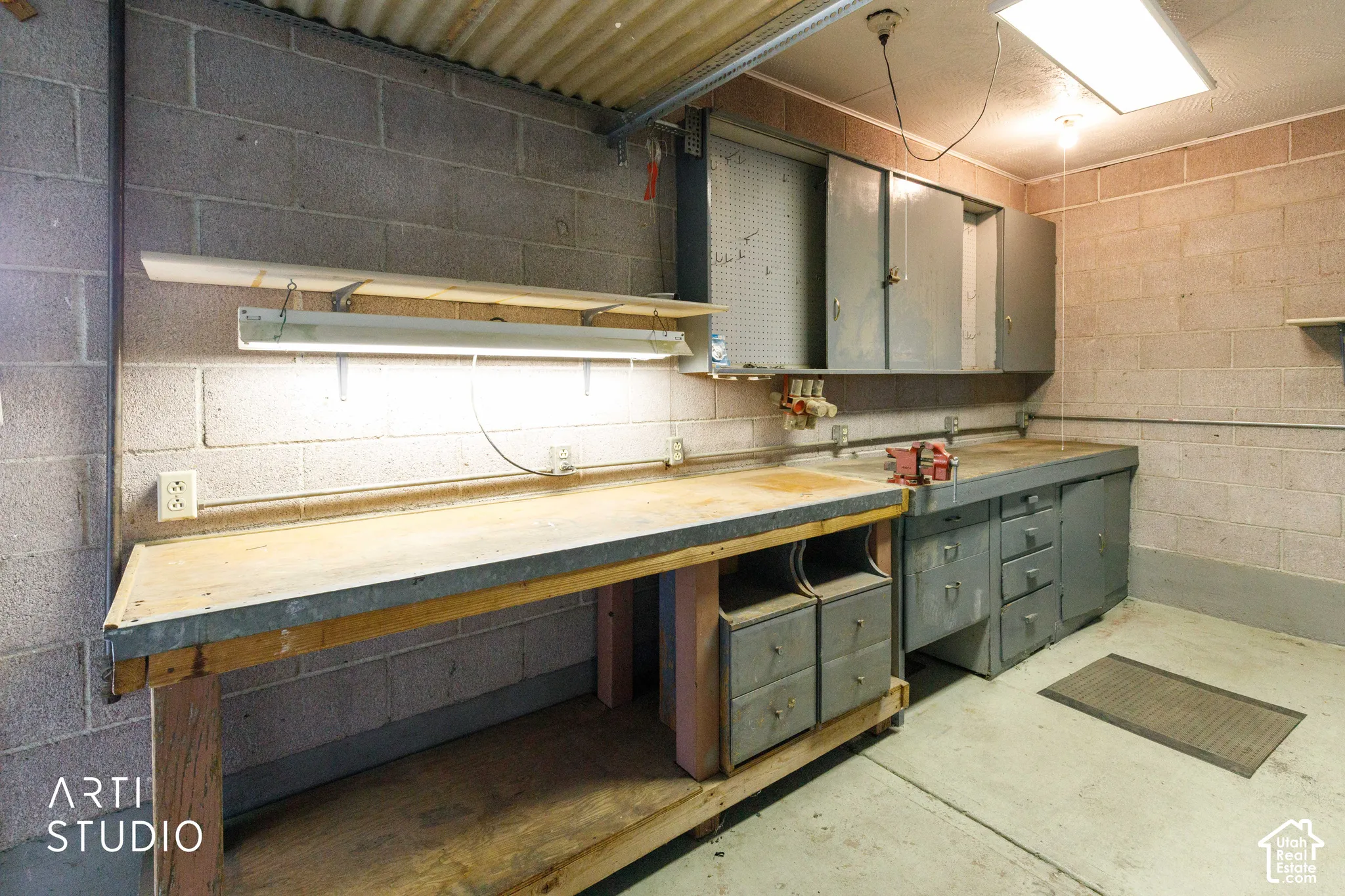 Workshop featuring concrete block walls, overhead fluorescent lighting, and built-in workbenches with storage