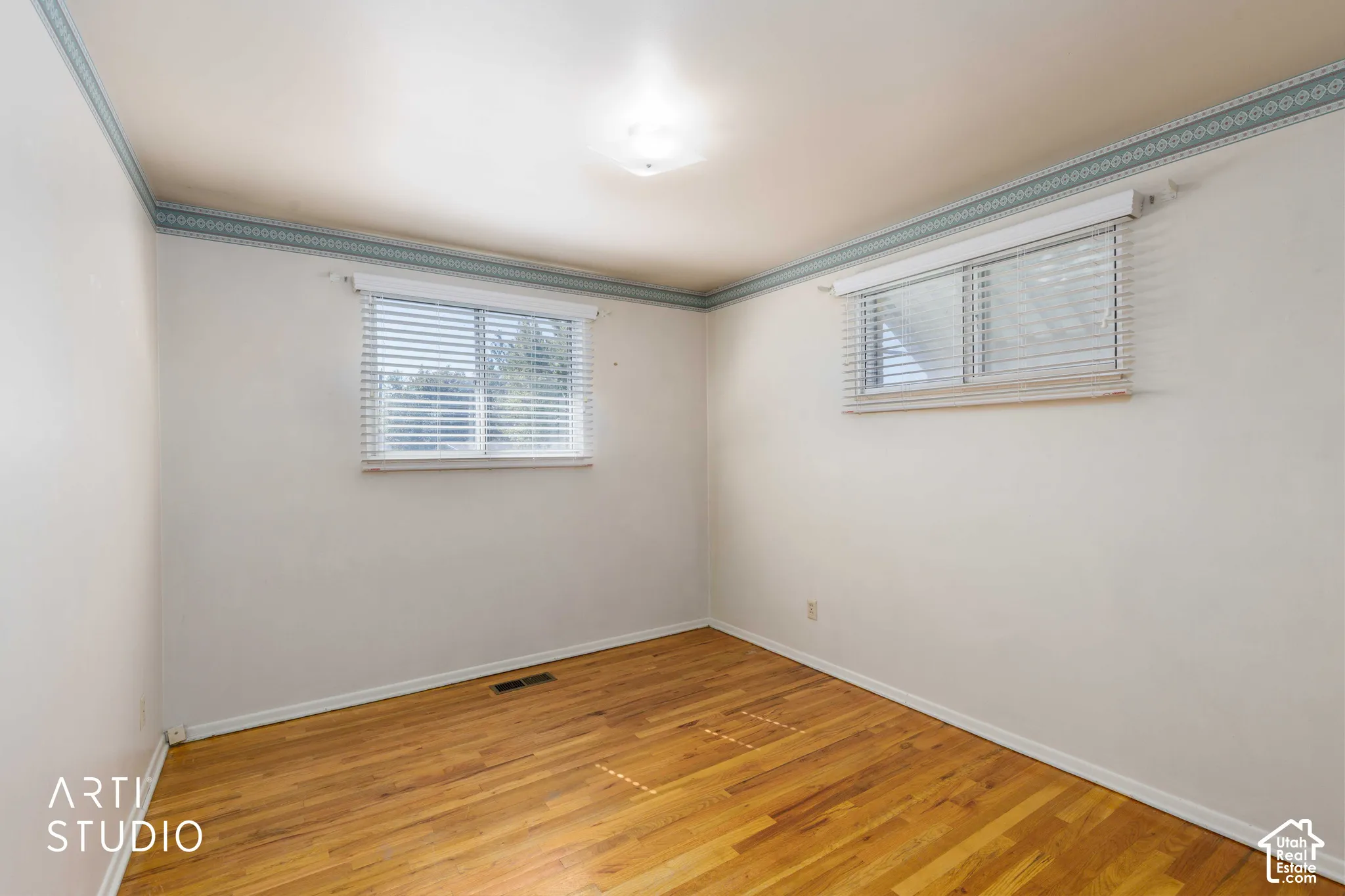 Wood-finish flooring, two windows with blinds, and white wall finishes