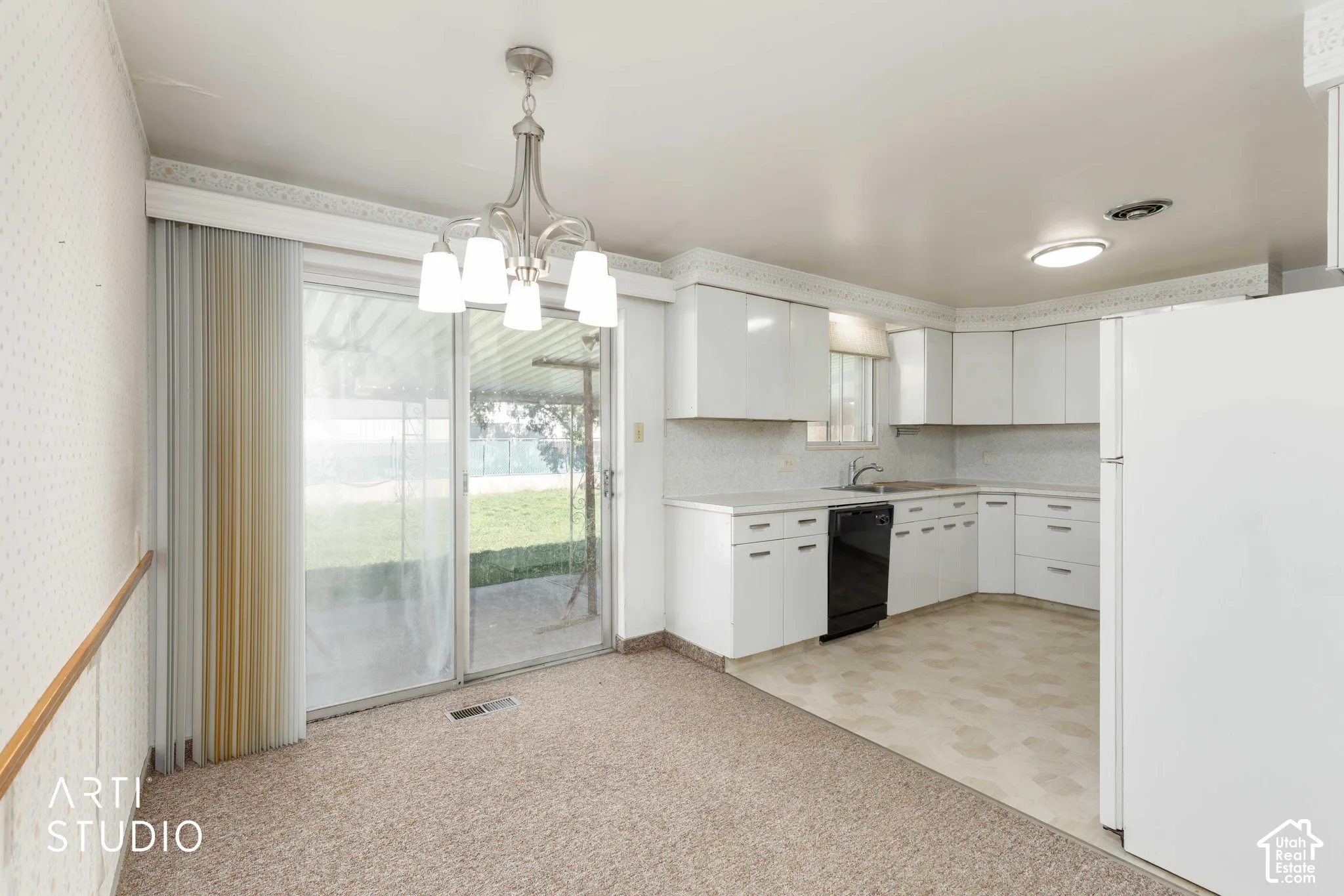 White kitchen cabinetry with black appliances, adjacent to a dining area with carpet flooring and a sliding glass door