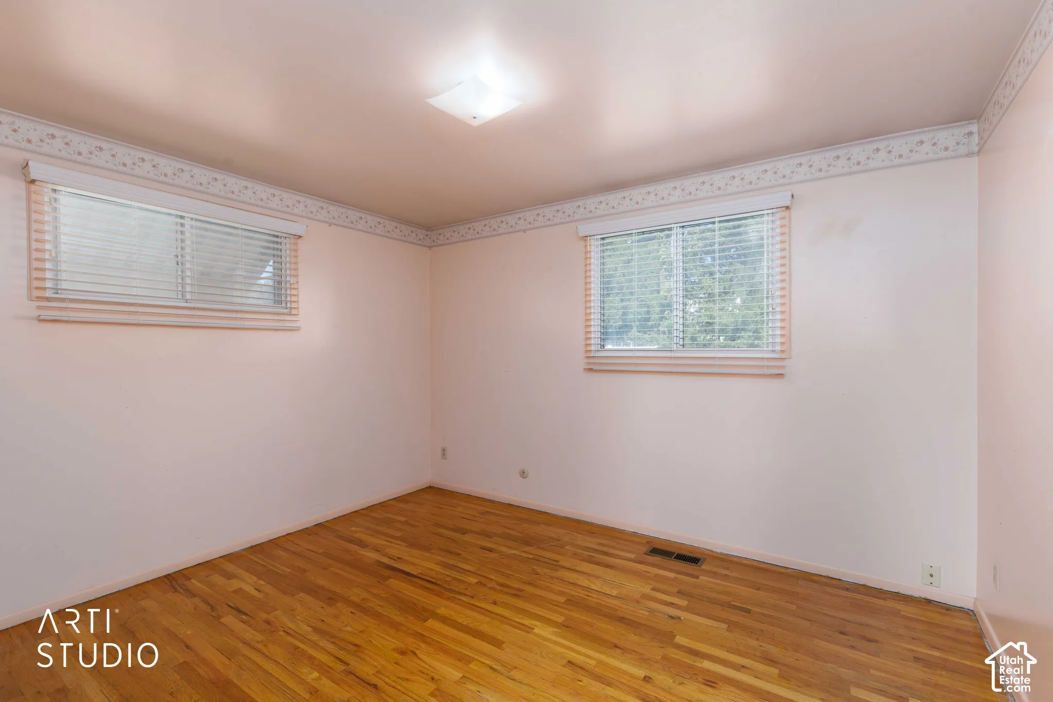 Wood-finish flooring with two windows, each featuring white blinds