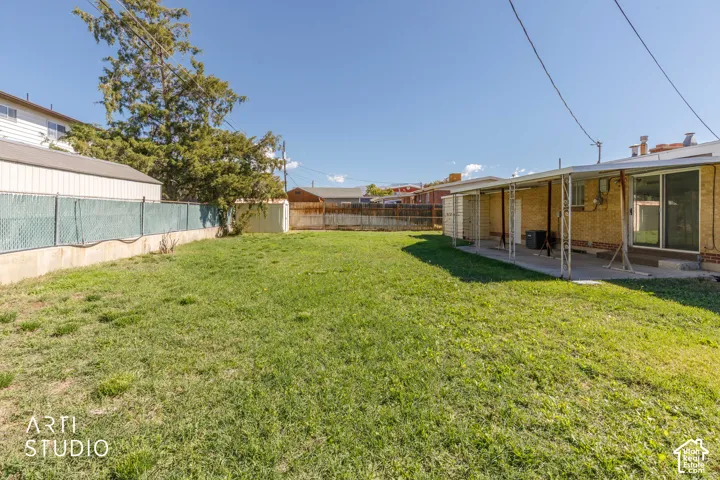 Expansive grassy backyard with a covered patio, chain-link fencing, and a storage shed