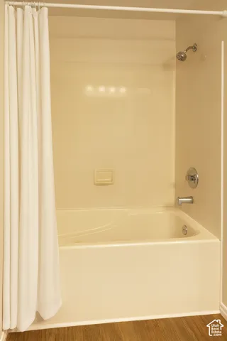 Built-in bathtub with integrated shower, chrome fixtures, and wood-finish flooring