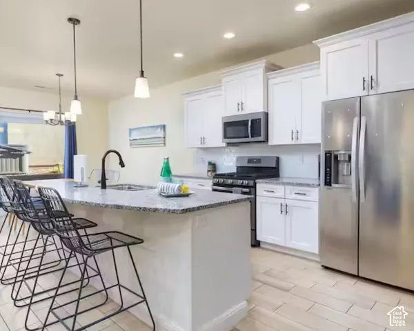 Kitchen featuring an island with a sink and pendant lighting, white cabinetry, stainless steel appliances, and light-toned tile flooring
