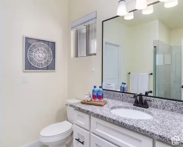 White shaker-style vanity with dark hardware, granite countertop, undermount sink, and a framed mirror with a four-light fixture