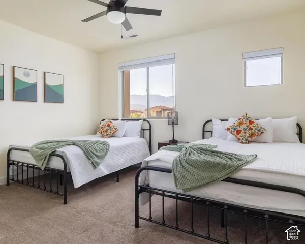 Carpeted flooring, two windows with window coverings, ceiling fan with light, and light-colored walls