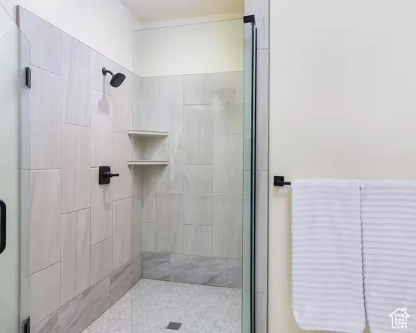 Glass-enclosed shower with matte black fixtures, integrated shelving, and a mosaic tile floor