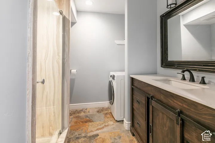 Stone tile flooring, wood-finish vanity with countertop, framed mirror, and glass-enclosed shower with stone-look wall panels