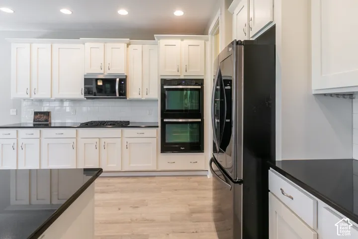 White shaker cabinetry, dark countertops, a stainless steel refrigerator, and a built-in double oven