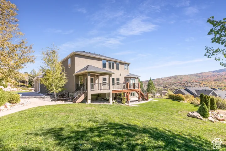 Expansive backyard featuring a manicured lawn, multi-level wood deck, covered patio, and distant mountain scenery
