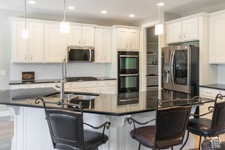 Kitchen featuring white cabinetry, dark countertops, stainless steel appliances, a dual wall oven, and a walk-in pantry