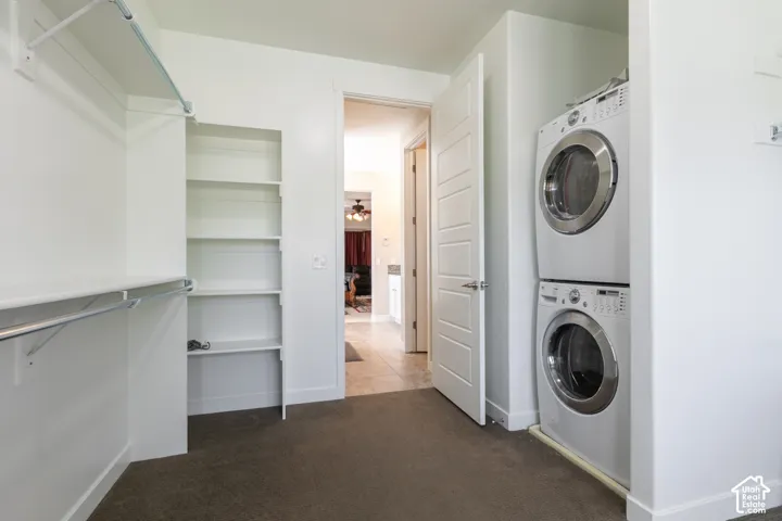 Built-in shelving, closet hanging rod, stacked laundry appliances, panel interior door, and carpet flooring