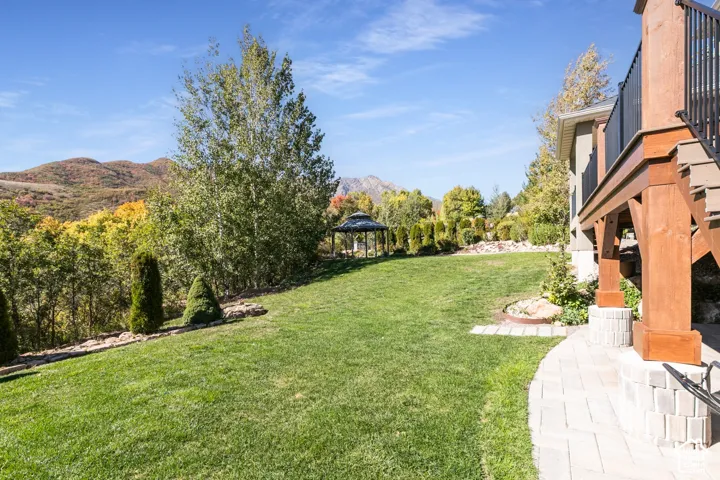 Expansive grassy yard with mature trees, a paved pathway, and a distant gazebo