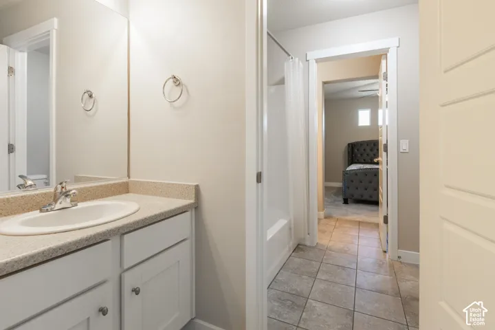 Vanity with an integrated sink and light-colored countertop, white shaker-style cabinetry, a built-in bathtub with shower, and tile flooring