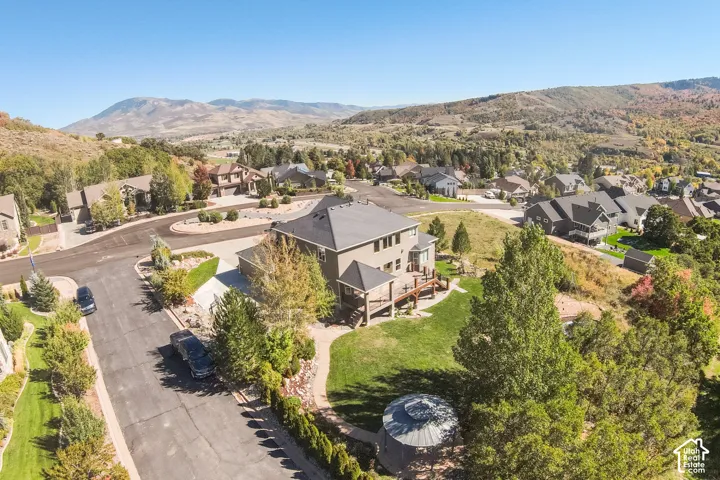 Contemporary residential architecture featuring a multi-level deck, expansive green lawn, mature trees, and a mountain backdrop