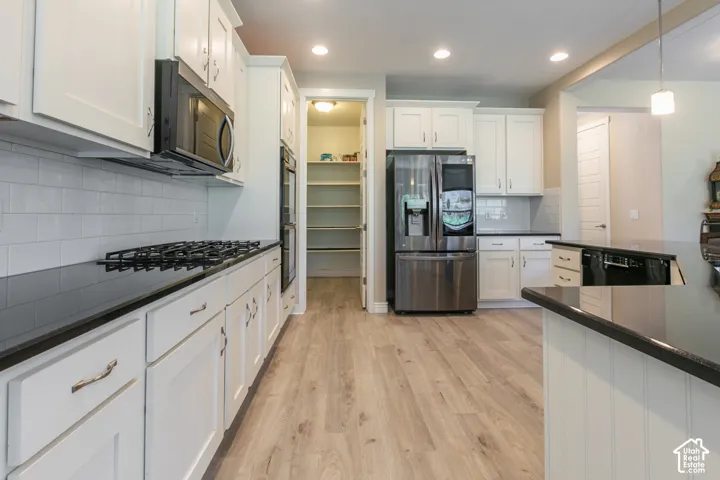 Kitchen featuring white cabinetry, dark countertops, a stainless steel refrigerator, a built-in microwave, and wood-finish flooring