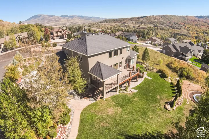 Multi-level exterior deck, covered patio, manicured lawn, and decorative stone-paved landscaping