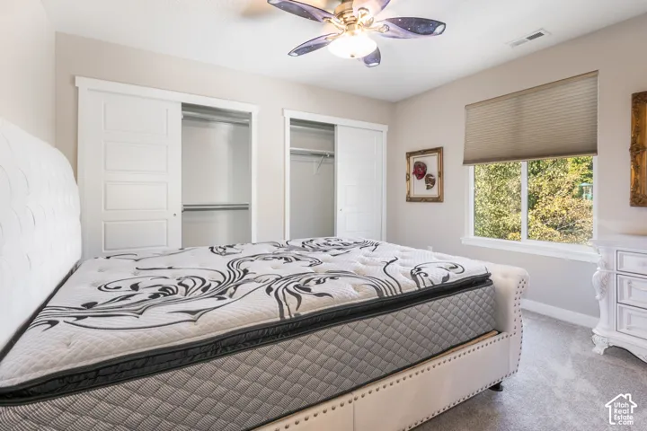 Wall-to-wall carpeting, window with cellular shades, ceiling fan with integrated lighting, and two sliding closet doors