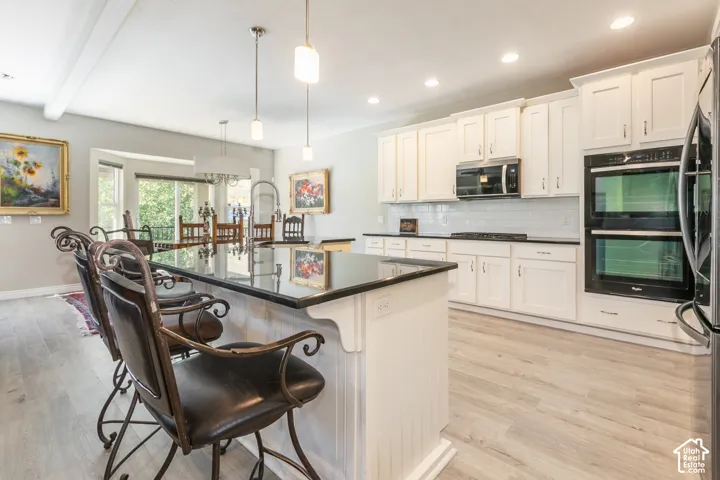 Expansive kitchen featuring a center island with bar seating, white cabinetry, dark countertops, and integrated double ovens