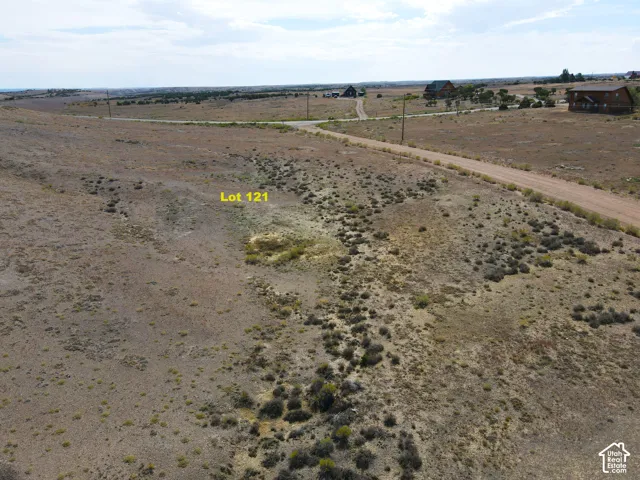 Expansive vacant lot featuring natural terrain and distant structures, with a visible unpaved road