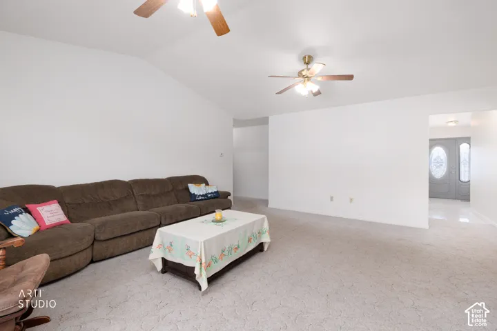 Vaulted ceiling with a ceiling fan, light-toned carpeting, and a second ceiling fan at the room's opposing end