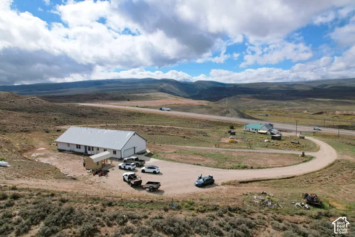 Expansive property featuring a metal roof building, covered porch, gravel driveway, and a distant mountain backdrop