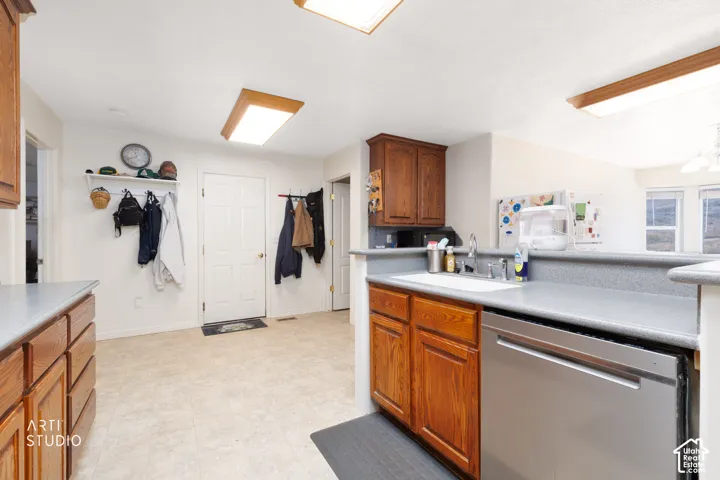Kitchen area featuring a stainless steel dishwasher, light wood-finish cabinetry, and solid surface countertops
