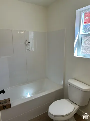 White acrylic bathtub with integrated shower surround, white toilet, and window with a white frame