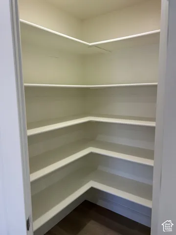 Corner pantry with multiple white shelves and dark wood-finish flooring