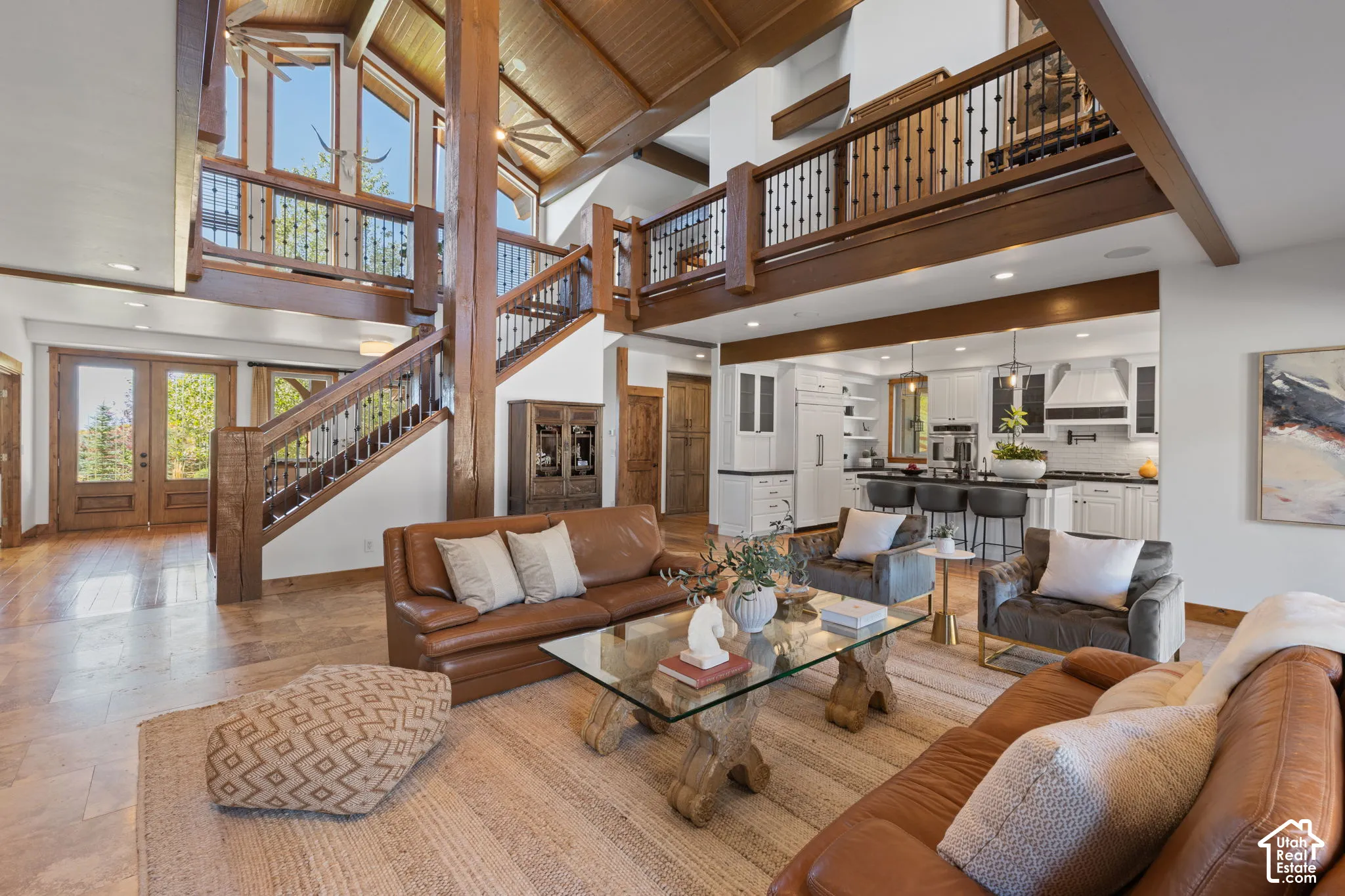 Vaulted wood-finish ceilings, an open-concept living space, a kitchen with a large island, and a prominent staircase with a wrought-iron baluster