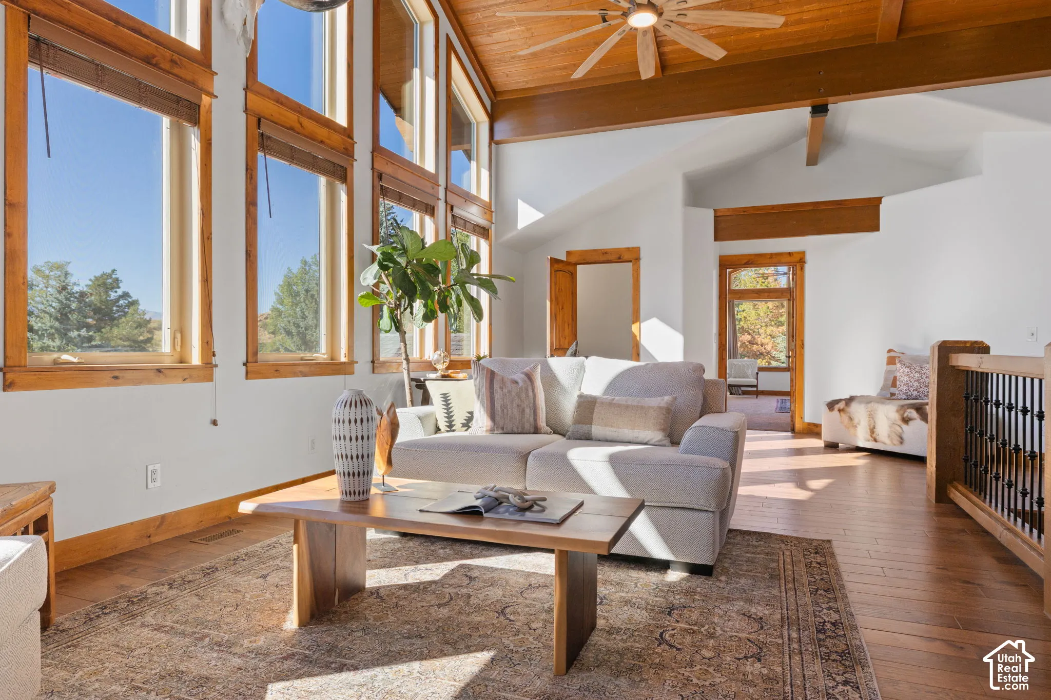 Vaulted ceiling with wood-finish planks and exposed beams, wood-finish flooring, full-height windows, and a ceiling fan