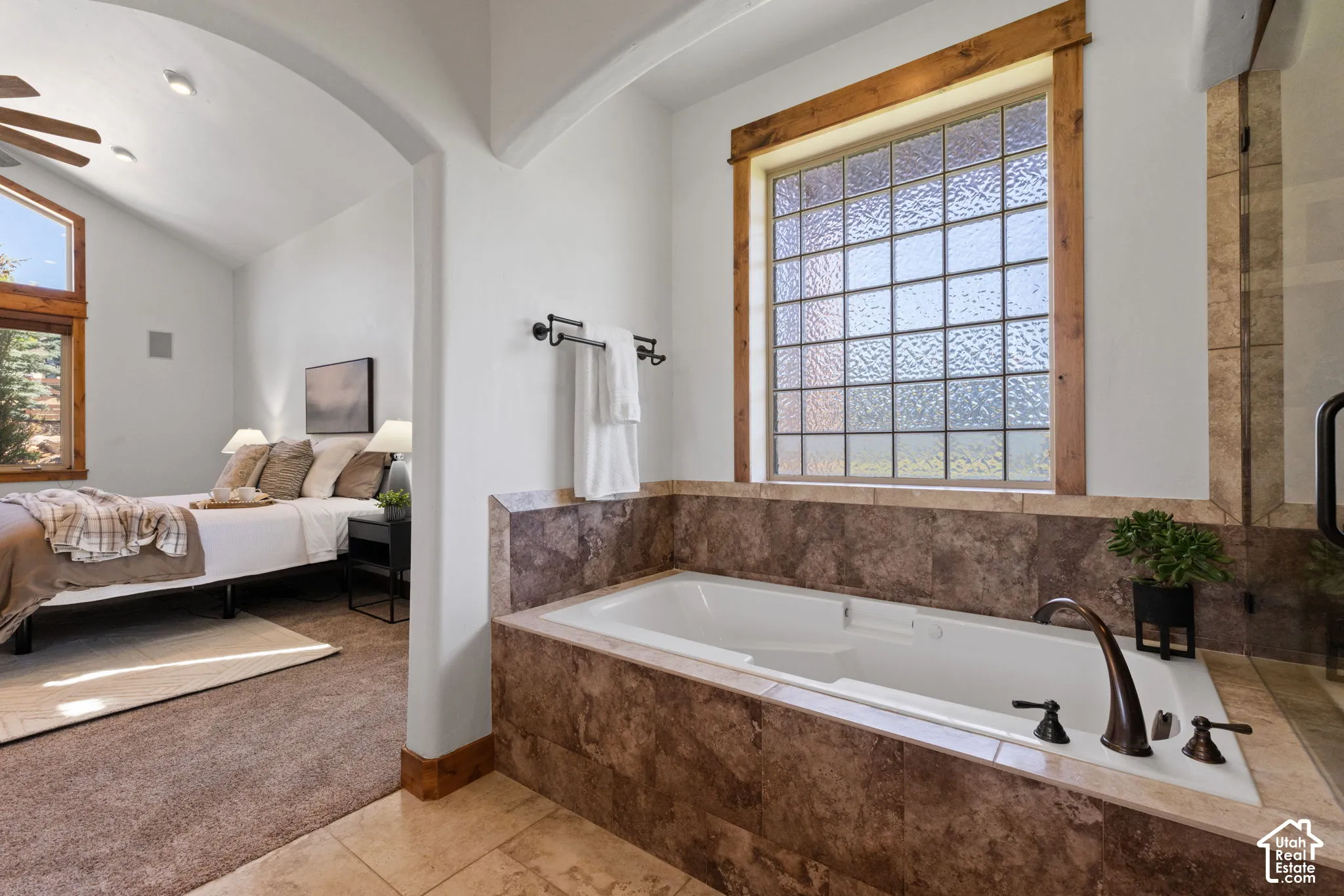 Soaking tub with bronze fixtures, tiled surround, and a glass block window