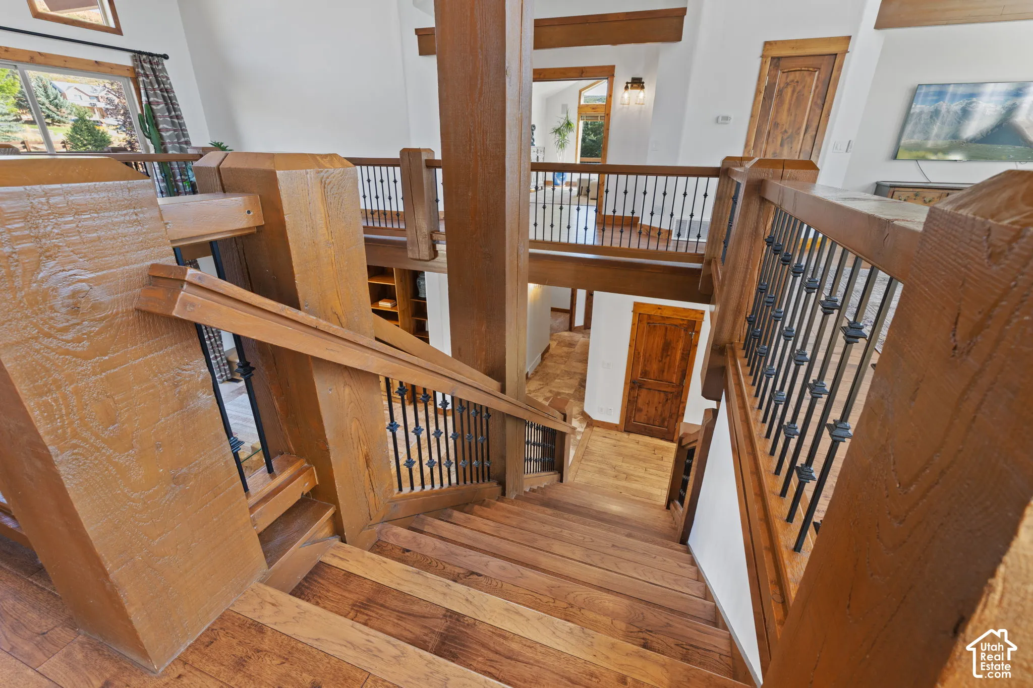Multi-level wood-finish staircase with wrought iron balusters, wood-finish flooring, and exposed wood beams