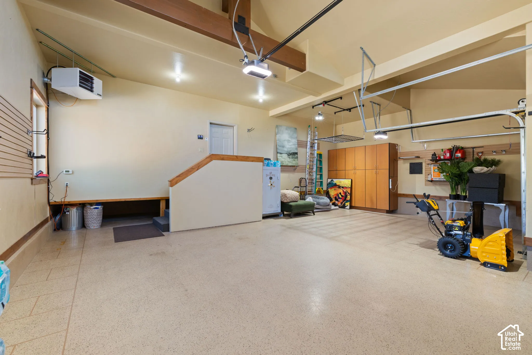 Spacious garage featuring a durable finished floor, built-in wooden cabinetry, wall-mounted storage tracks, a built-in bench, and exposed ceiling beams