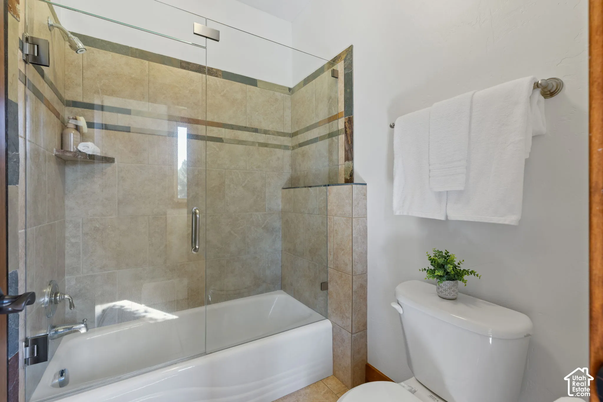 Bathtub with a glass shower enclosure, full tile surround, and a wall-mounted showerhead