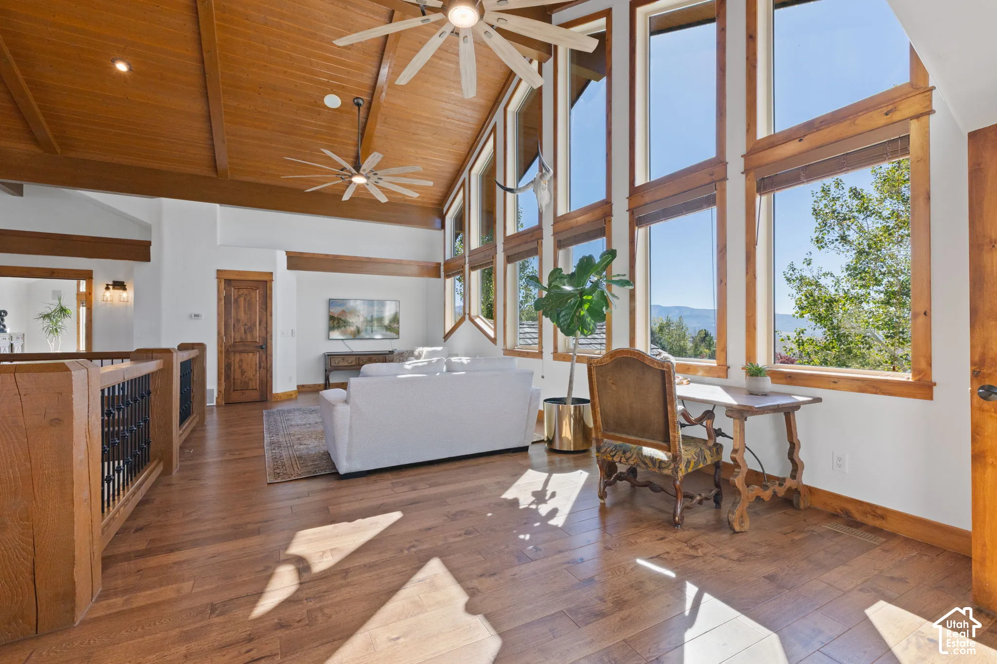 Vaulted wood-paneled ceilings, extensive window array, wood-finish flooring, exposed wood beams, and a wood railing with black metal spindles
